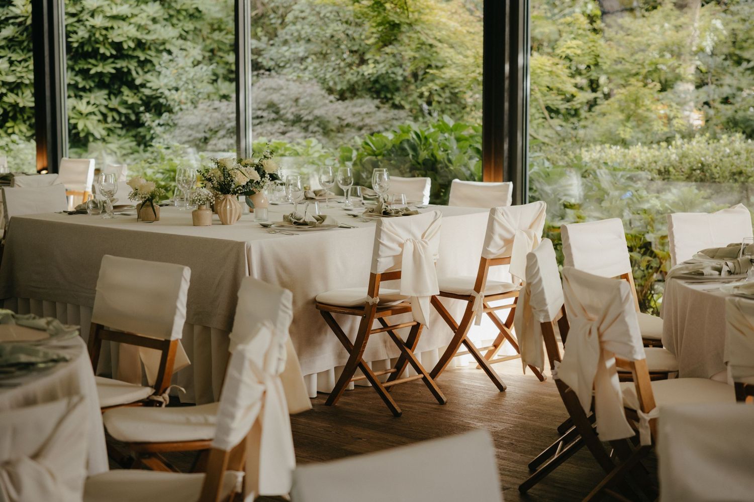 An airy wedding reception venue with white tablecloths and wooden chairs.