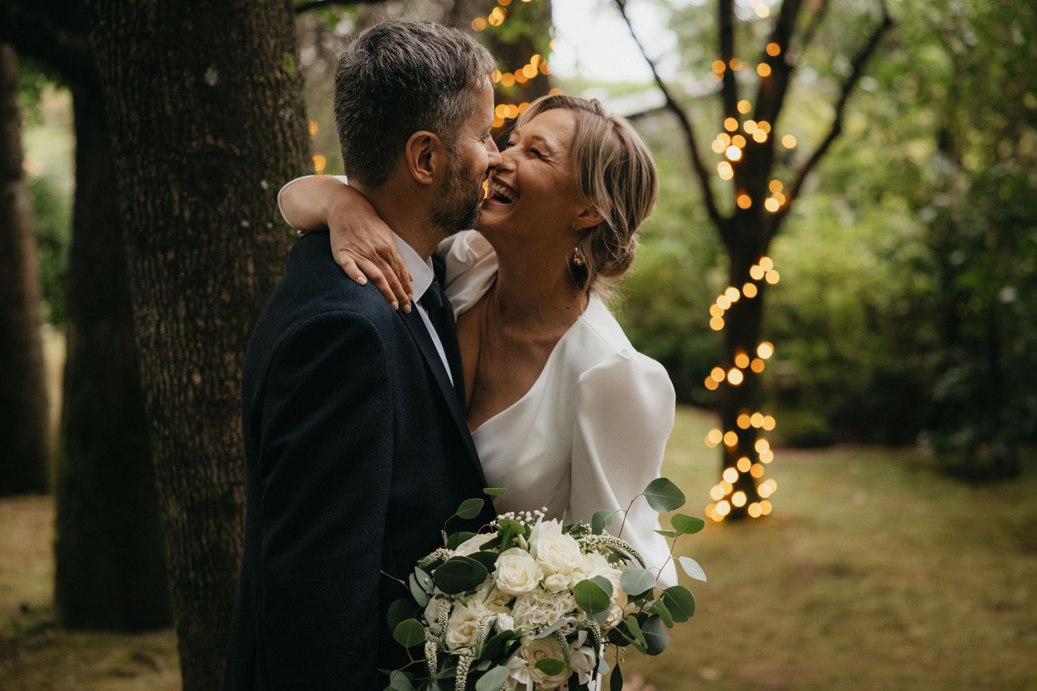 An intimate outdoor wedding moment with twinkle-lit trees in the background.