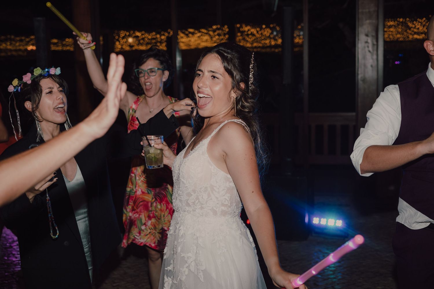 Wedding guests dance with light-up wands during nighttime celebration.