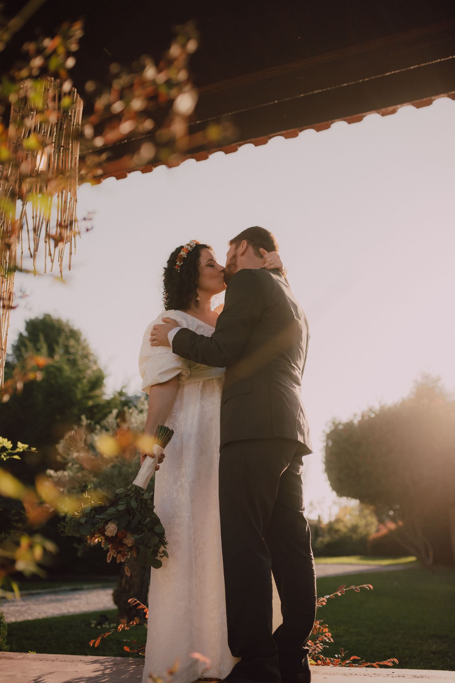 Intimate wedding moment captured under hanging floral arrangements at sunset.