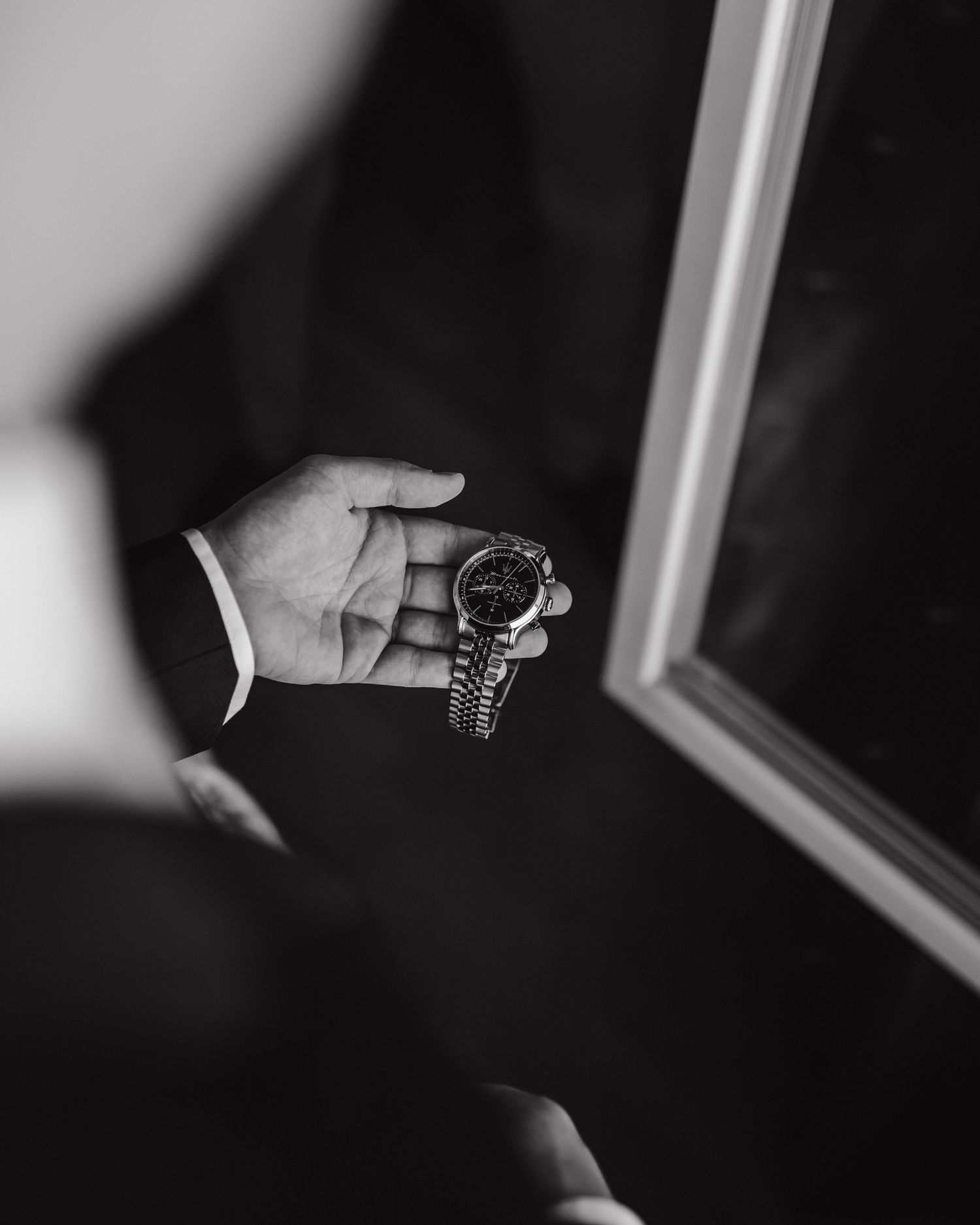 Black and white close-up of hand holding an elegant watch against mirror reflection.