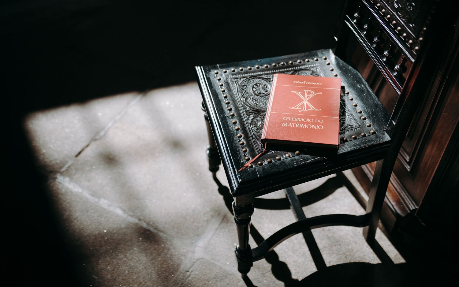 A red book rests on an ornate dark chair casting dramatic shadows.