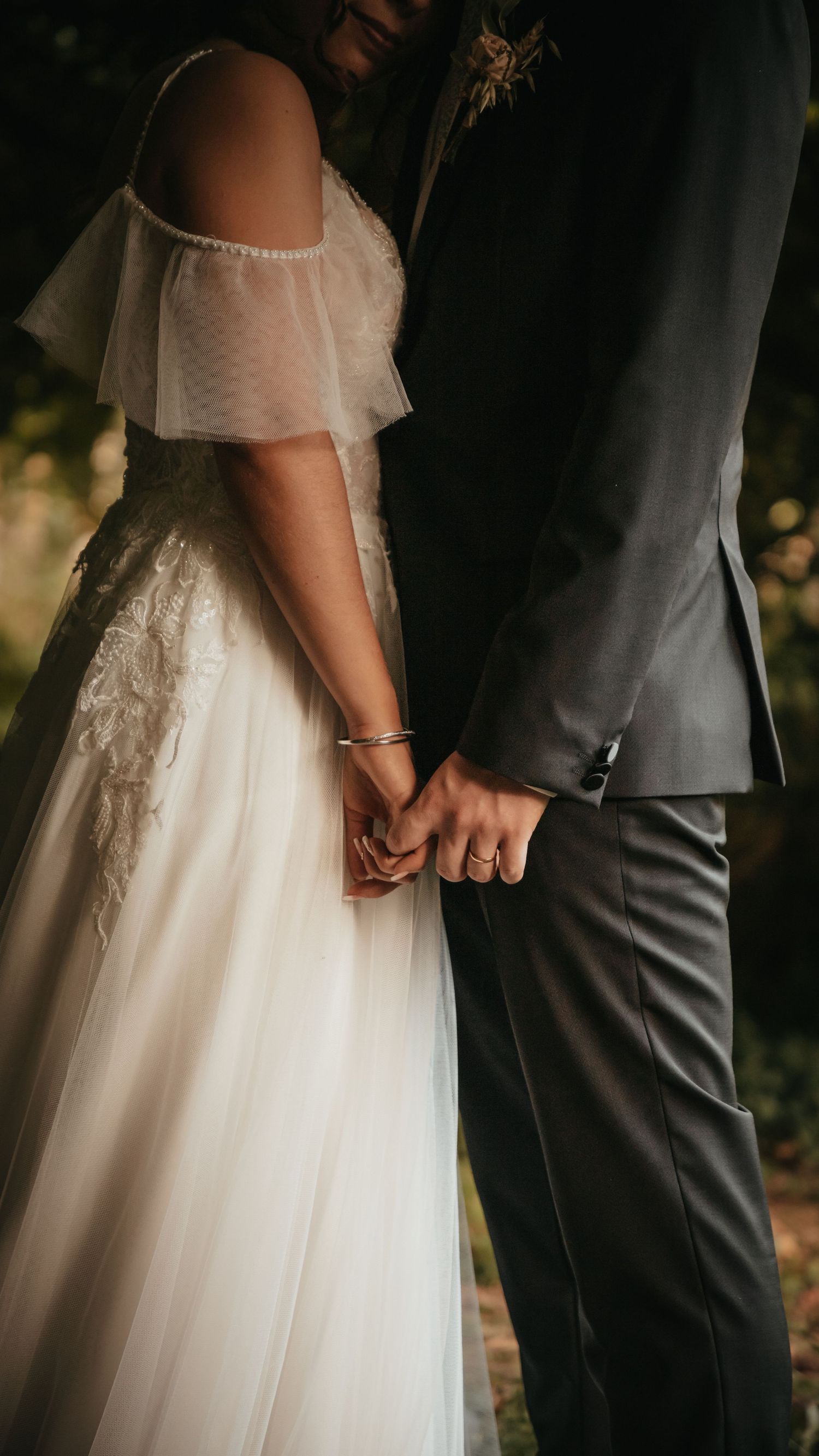 Detail shot of couple holding hands showing wedding dress and formal suit.