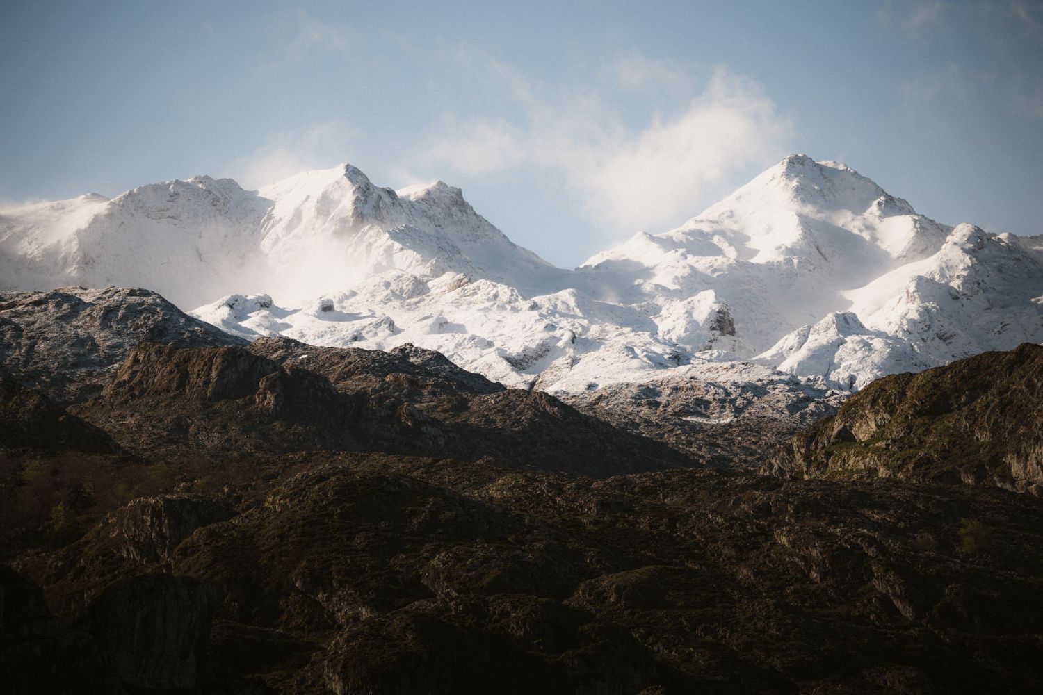 Majestic snow-covered mountain peaks tower over rocky terrain under a bright blue sky.
