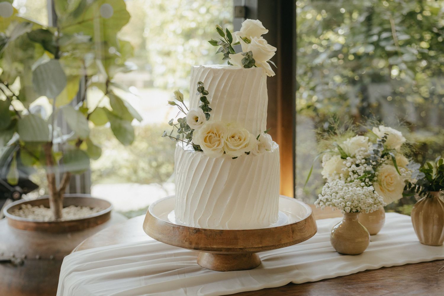 An elegant white wedding cake decorated with fresh flowers on a wooden cake stand.