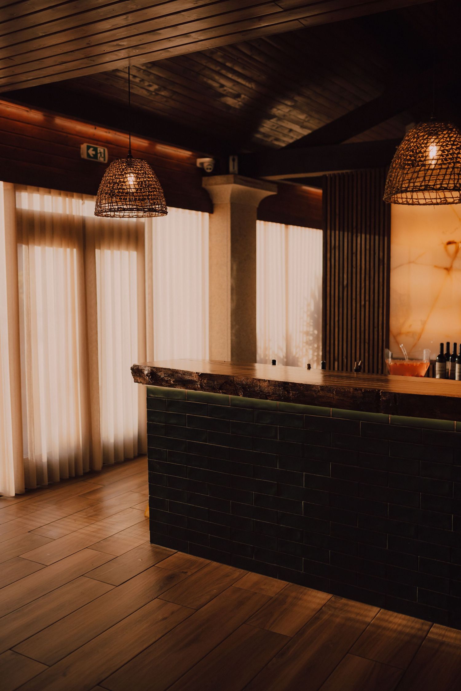 A modern bar area with woven pendant lights and white curtains in warm lighting.