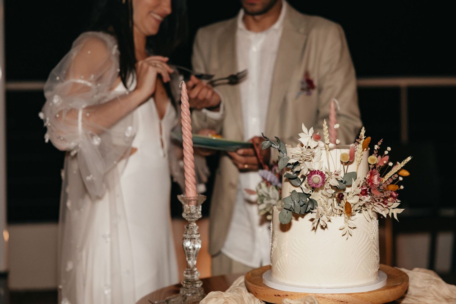 Couple cutting elegant white wedding cake decorated with dried flowers at reception.