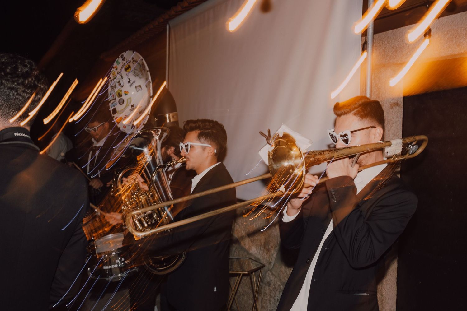 A brass band performs with trombones and trumpets at a nighttime event.