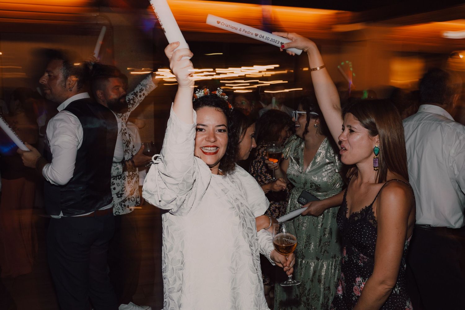 Wedding celebration with guests dancing and having fun under orange ambient lighting.