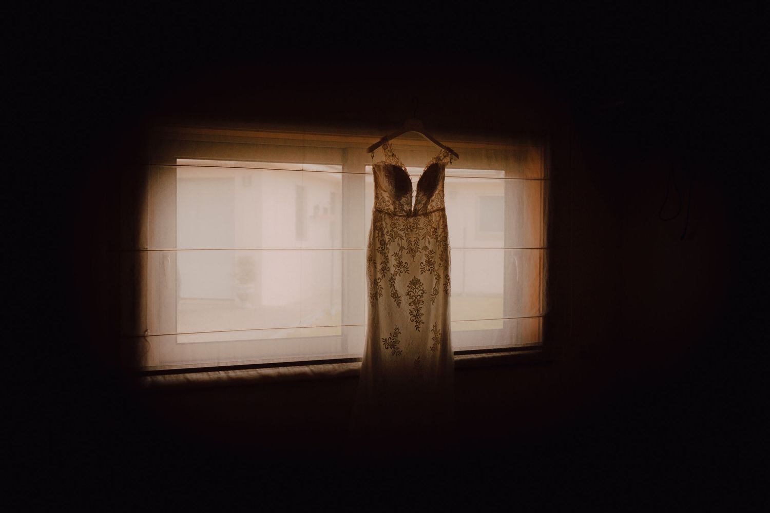 Wedding dress silhouetted against backlit window in dramatic lighting.