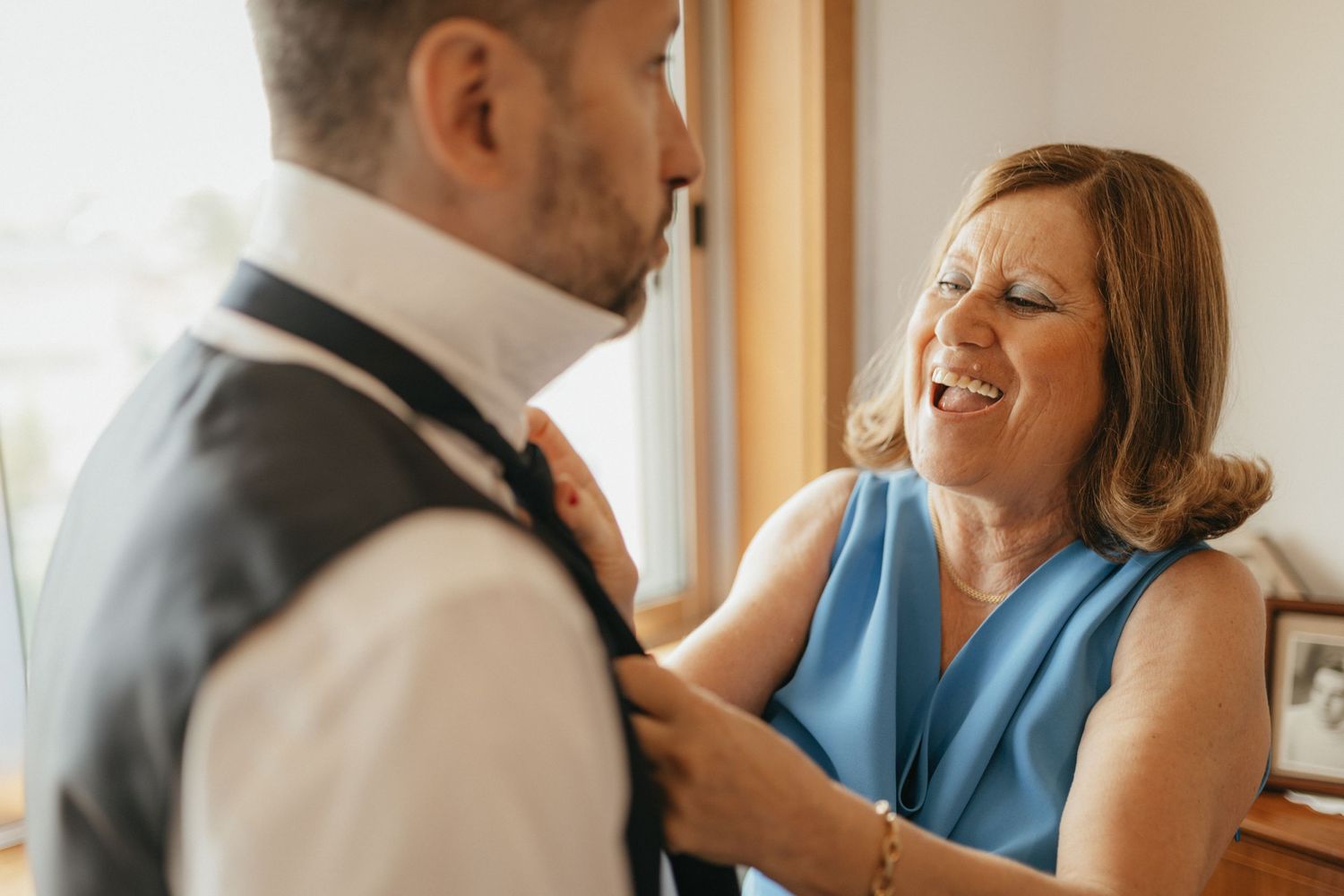 Intimate pre-wedding moment showing final adjustments to formal attire.