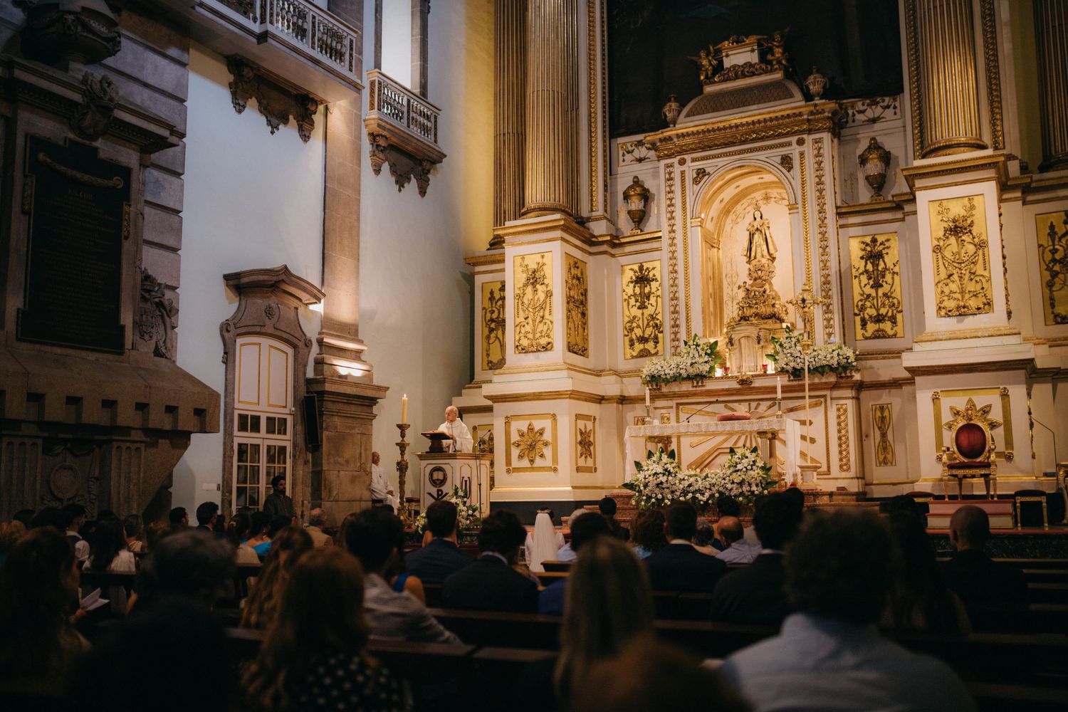 Interior of historic church with ornate gold altar and religious artwork illuminated by natural light.