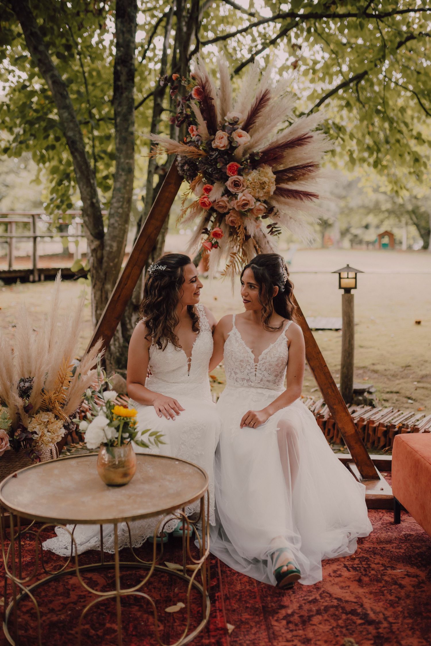 Newlyweds sit together under a boho-style wooden arch decorated with dried flowers and feathers.