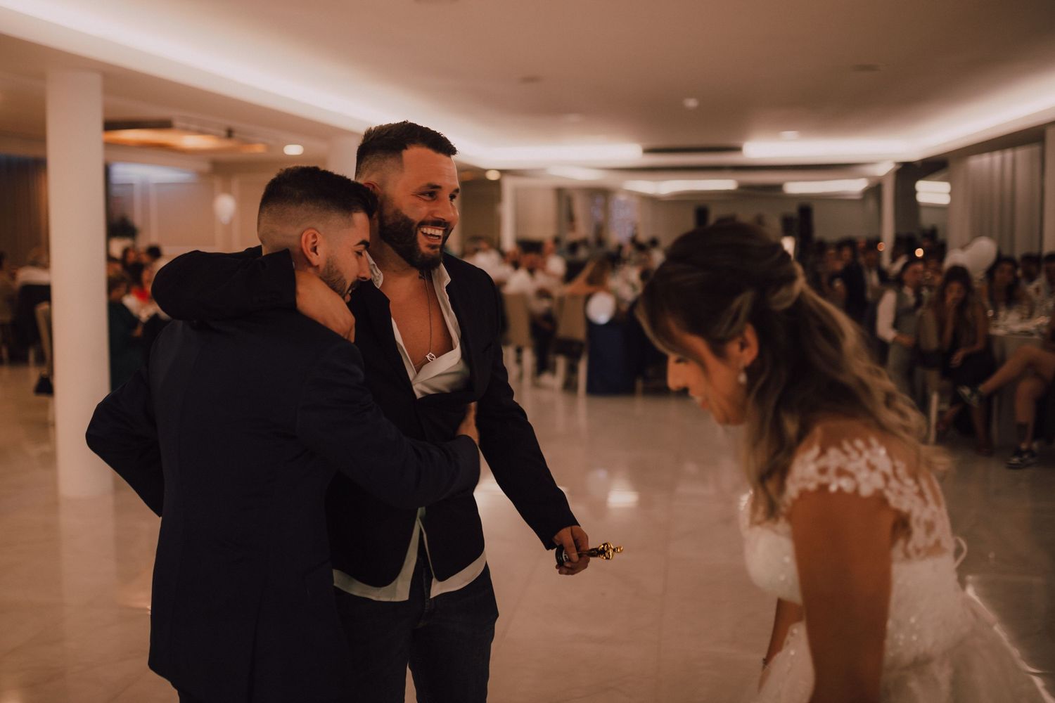 Wedding reception guests dancing and celebrating in a modern venue with ambient lighting.