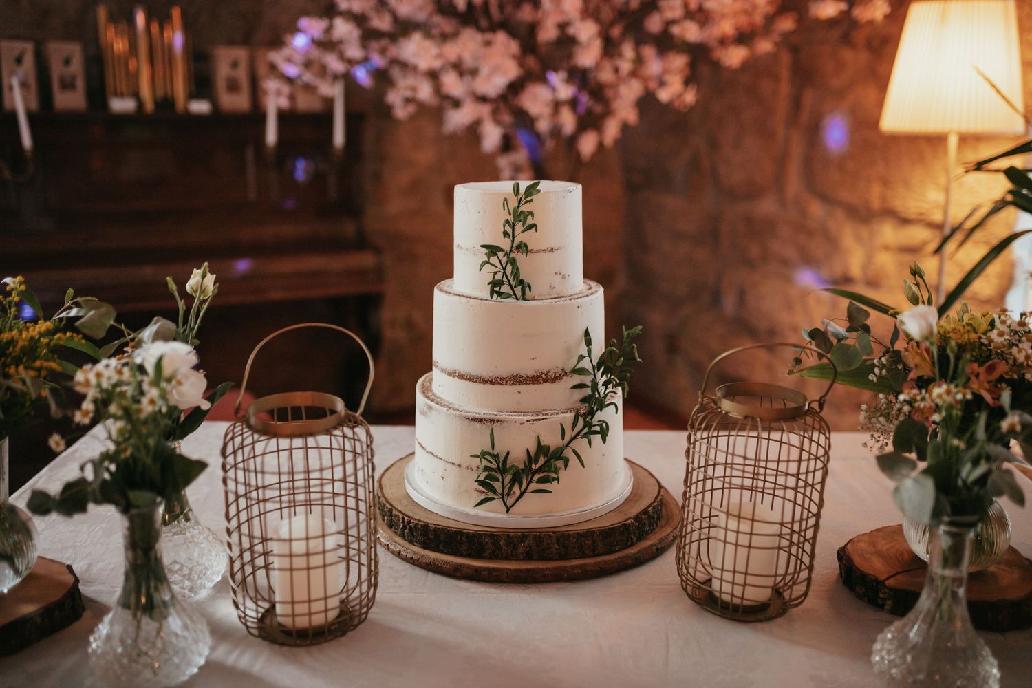 Elegant white tiered wedding cake decorated with greenery and surrounded by lanterns.
