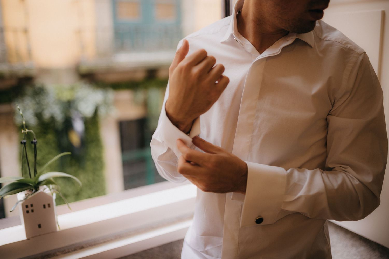 Close-up of someone adjusting white dress shirt cuffs near a window with natural light.
