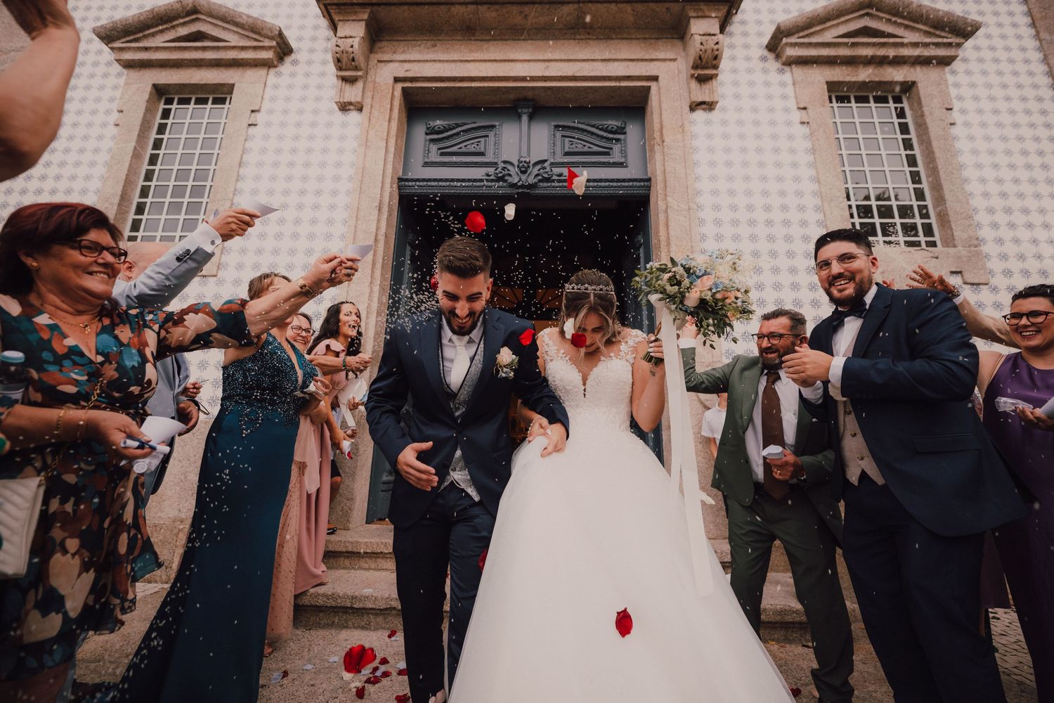 Festive wedding celebration on church steps with guests throwing rose petals.