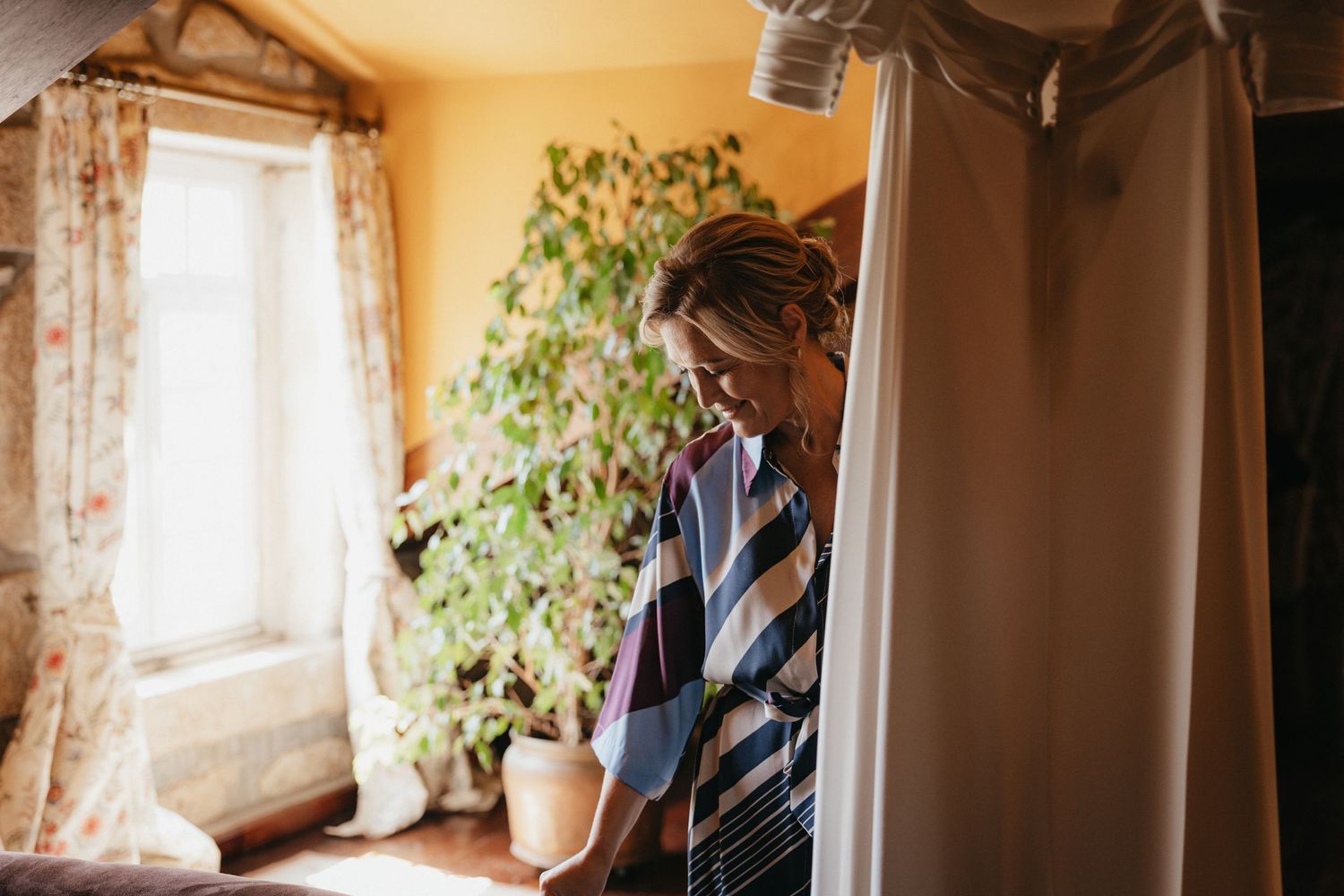Morning wedding preparations by window with indoor plants and natural lighting.