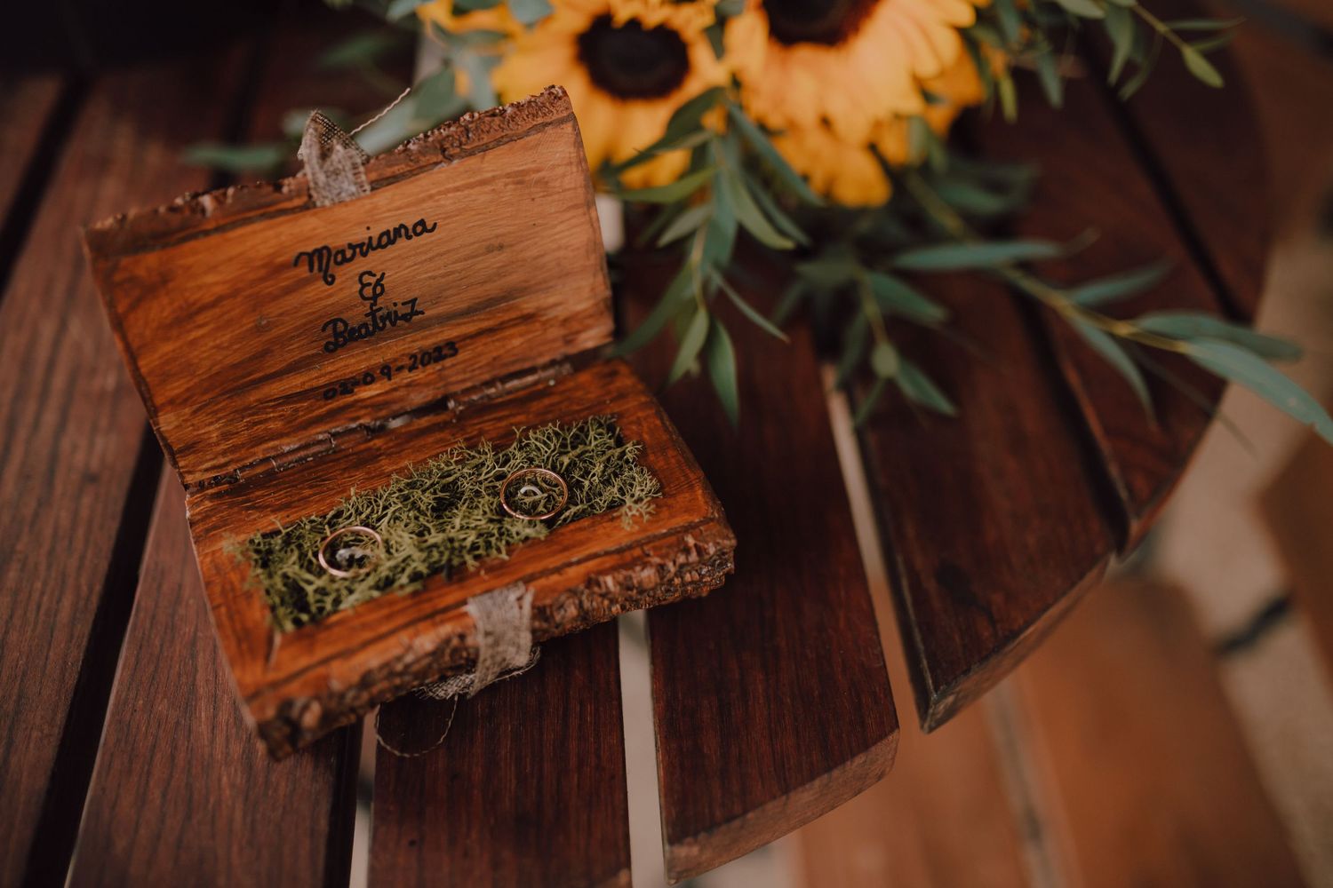 Rustic wooden box filled with greenery next to sunflowers on dark wooden surface.