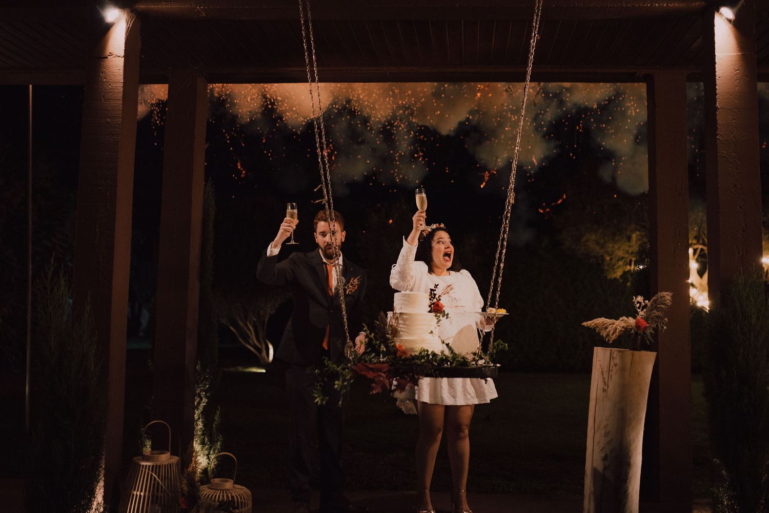 A couple enjoys a romantic moment on swings during their nighttime wedding reception.