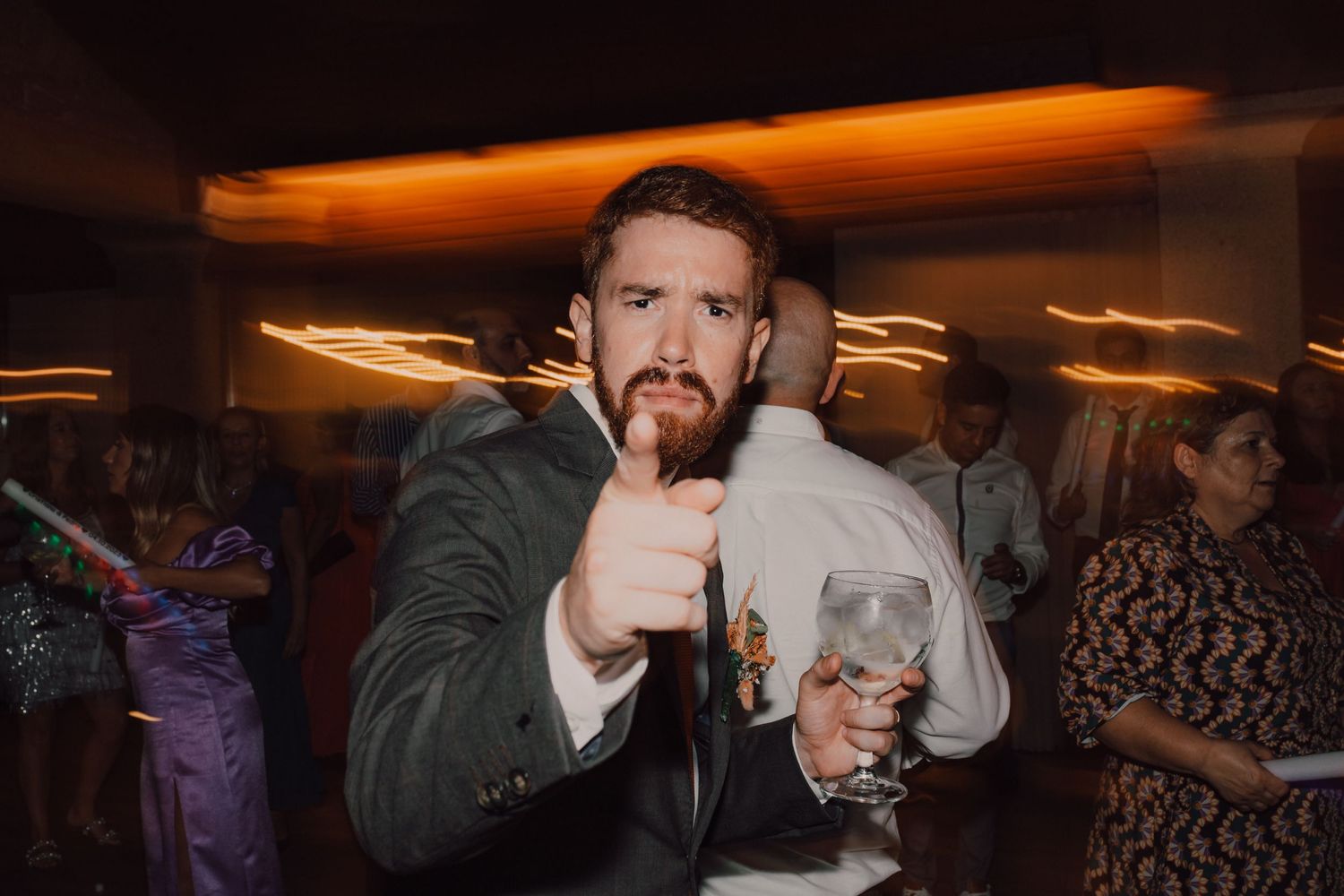 A lively wedding reception moment captured in motion under ambient orange lighting.