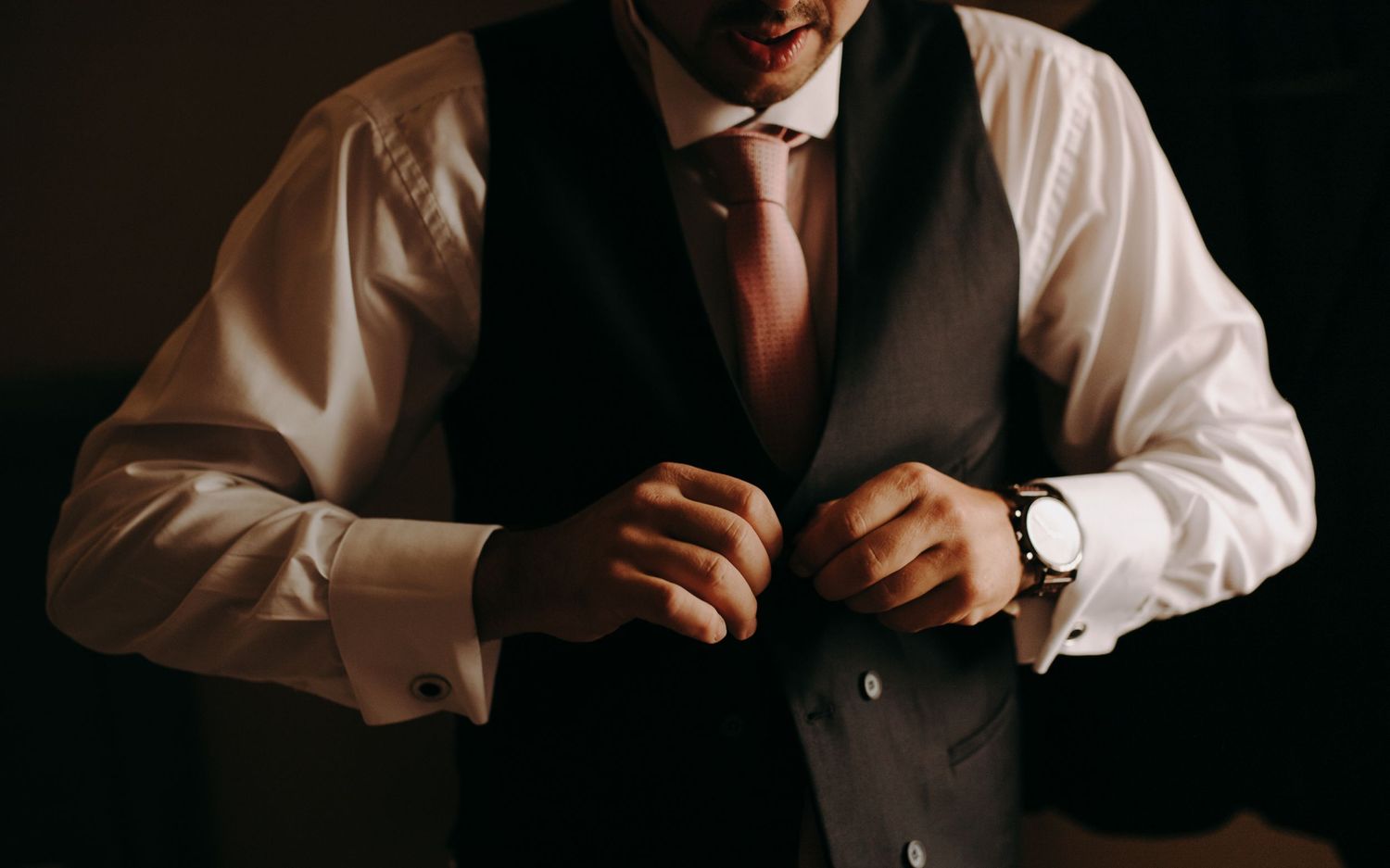 Close-up shot of formal attire showing a white dress shirt, black vest, and wristwatch.