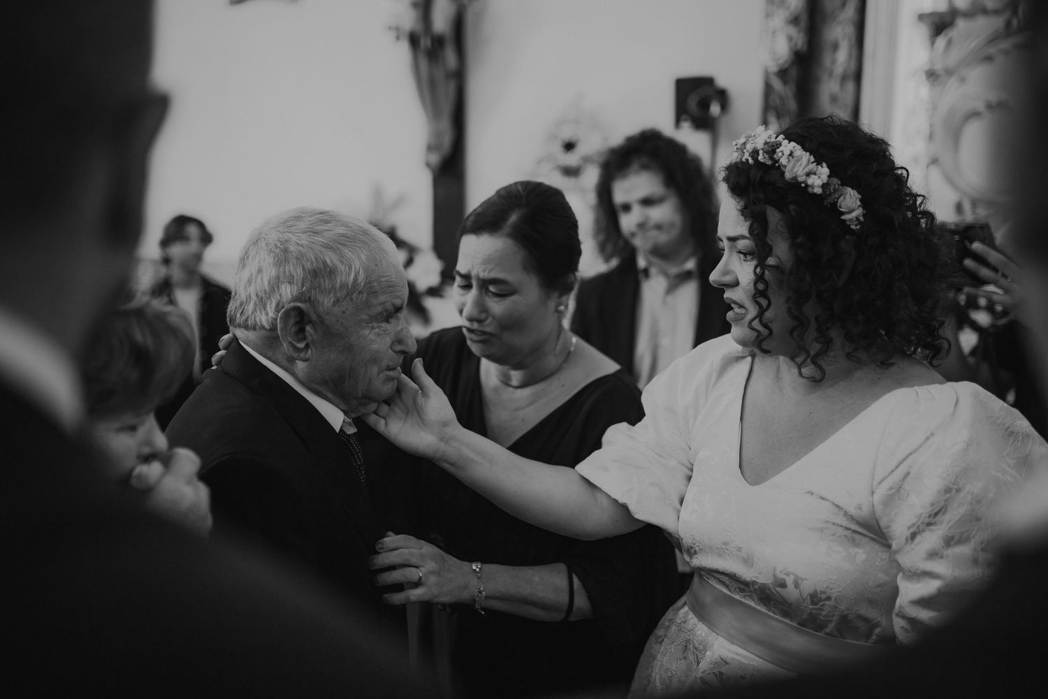 An emotional black and white wedding moment shows guests embracing in a traditional church setting.