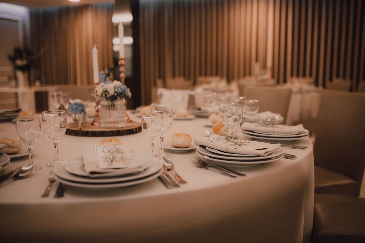 Elegant wedding reception table setting with stacked plates and floral centerpieces in a banquet hall.