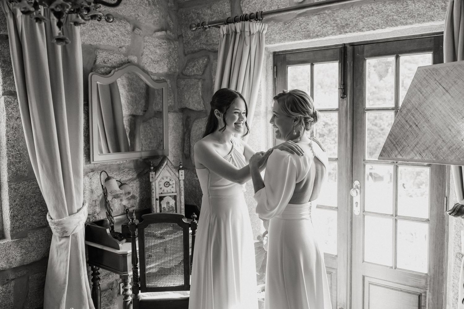 Two people helping with wedding preparations in an elegant room with stone walls and natural light.