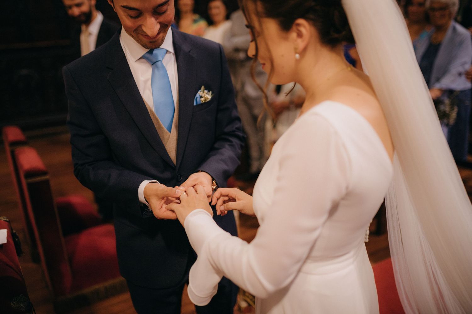 Close-up of wedding ring exchange during ceremony in church with red carpet.