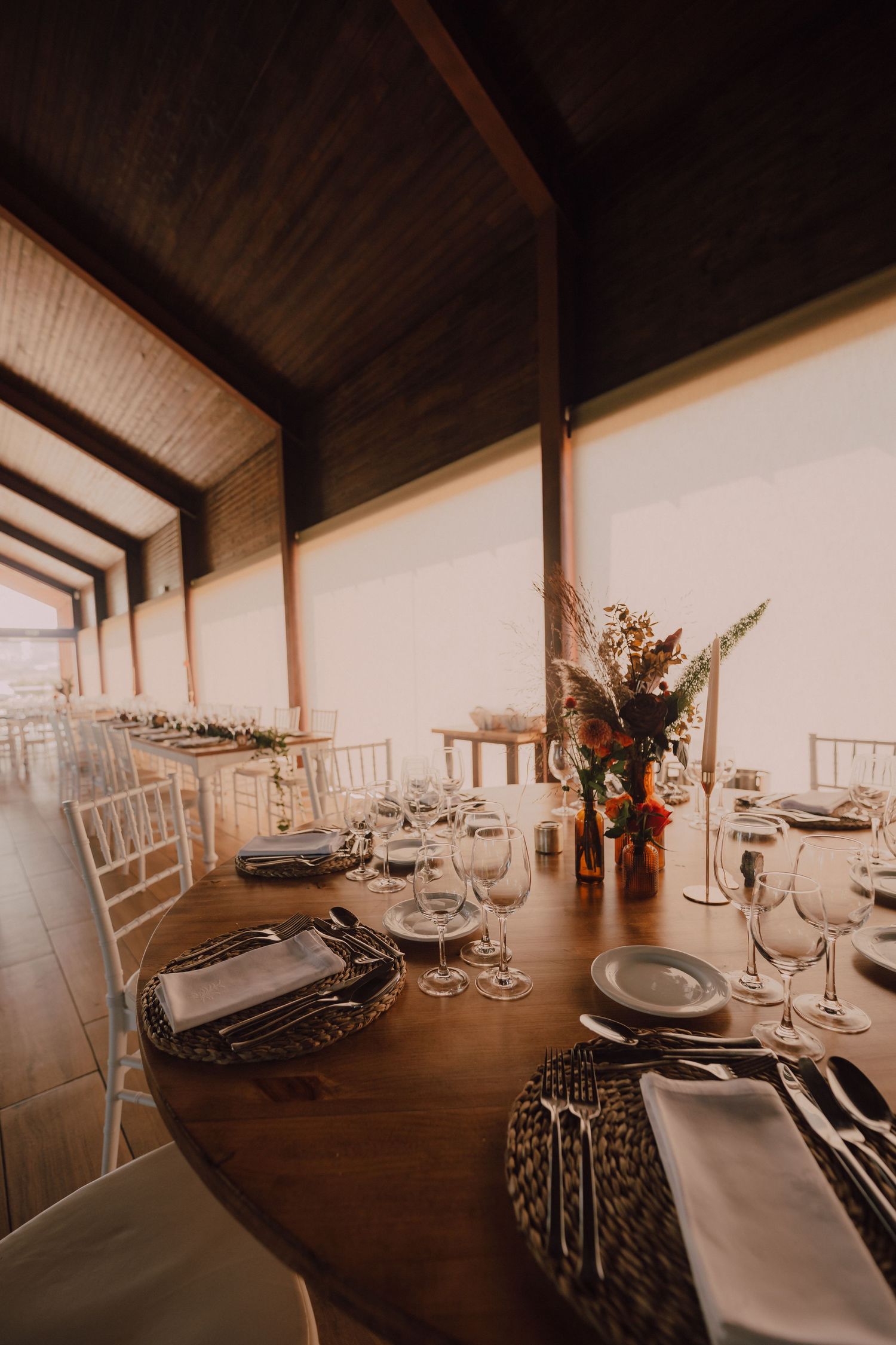 Rustic wedding reception setup with wooden tables, white chairs, and elegant place settings.