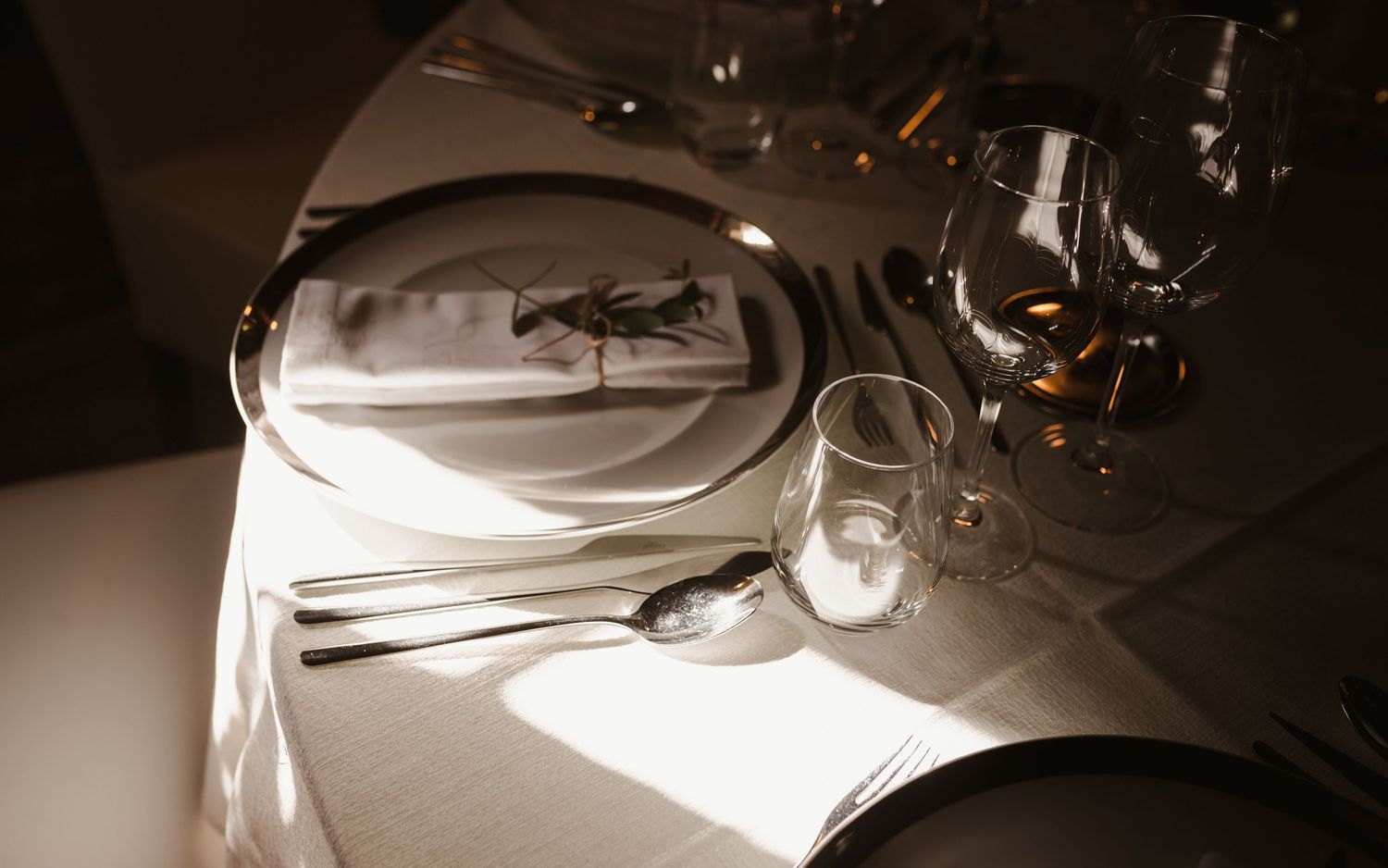 Elegant place setting with white plates and glassware in moody lighting.