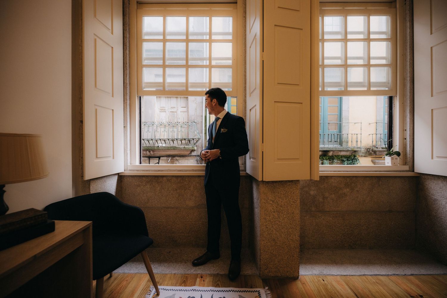 Silhouette of person in formal attire standing between two tall windows in elegant room.