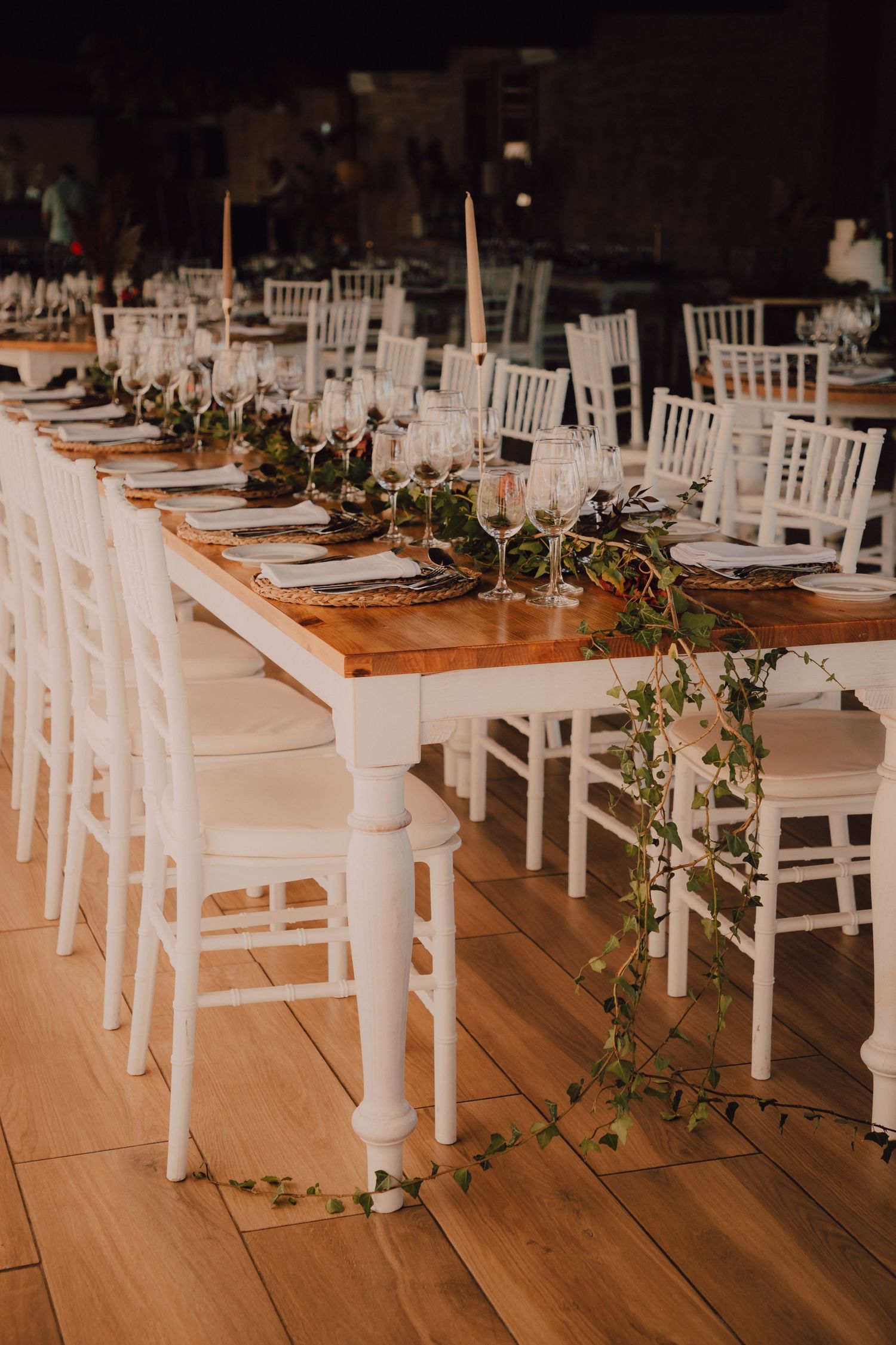 Elegant wedding reception table set with white chairs and greenery garland decorations.
