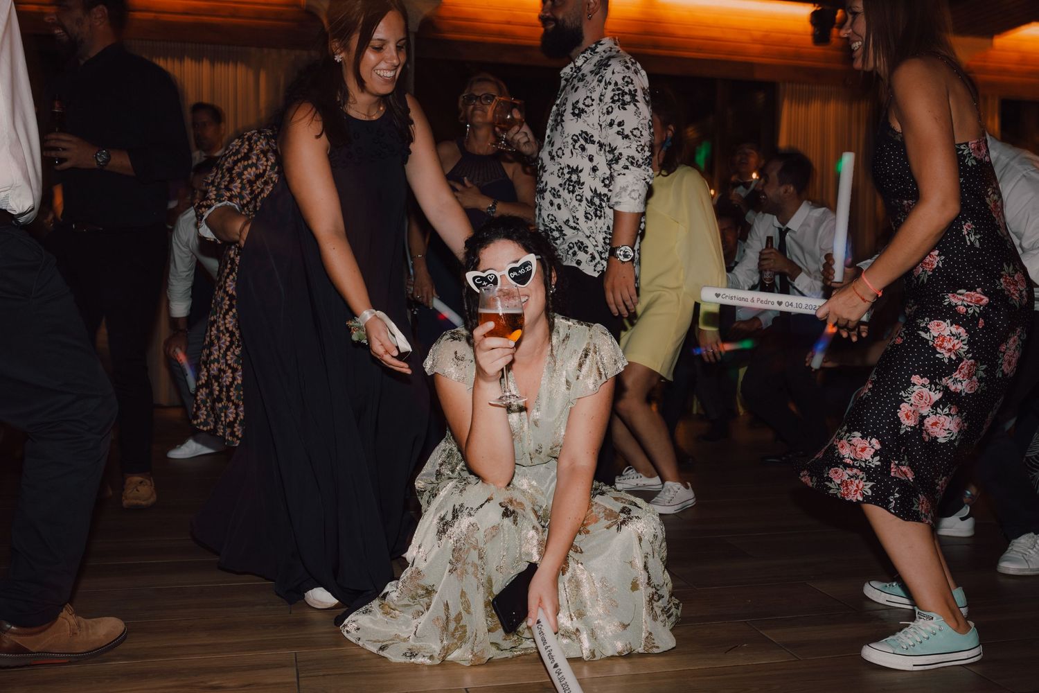 Reception guest dancing playfully on wooden dance floor surrounded by partygoers.