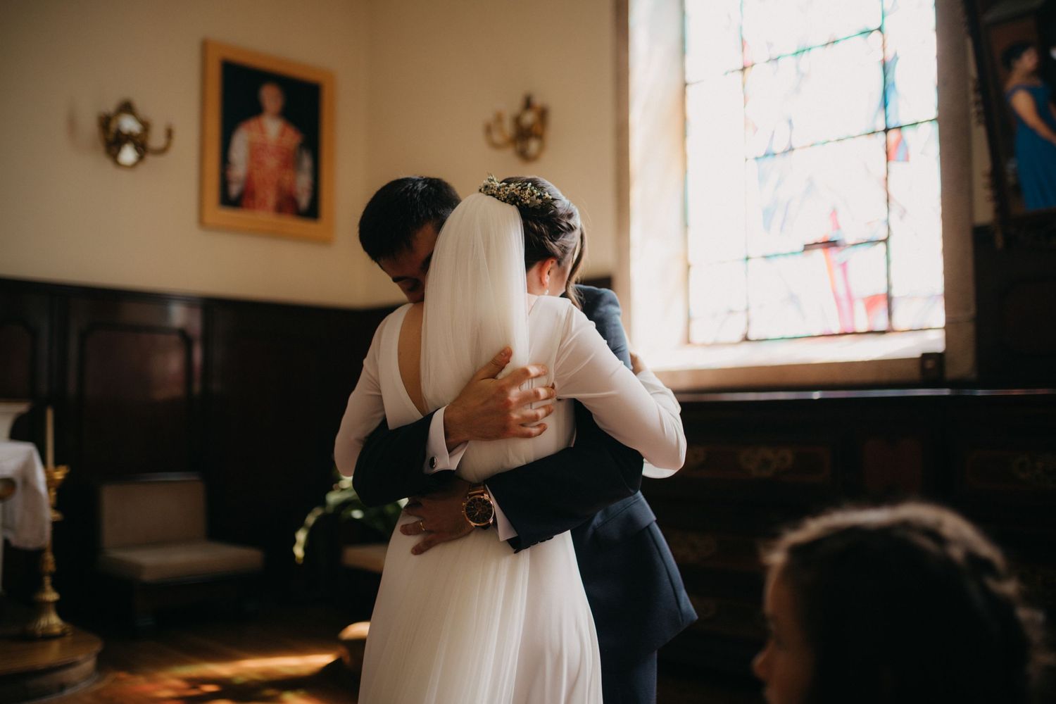 A tender embrace between newlyweds in front of a stained glass window.