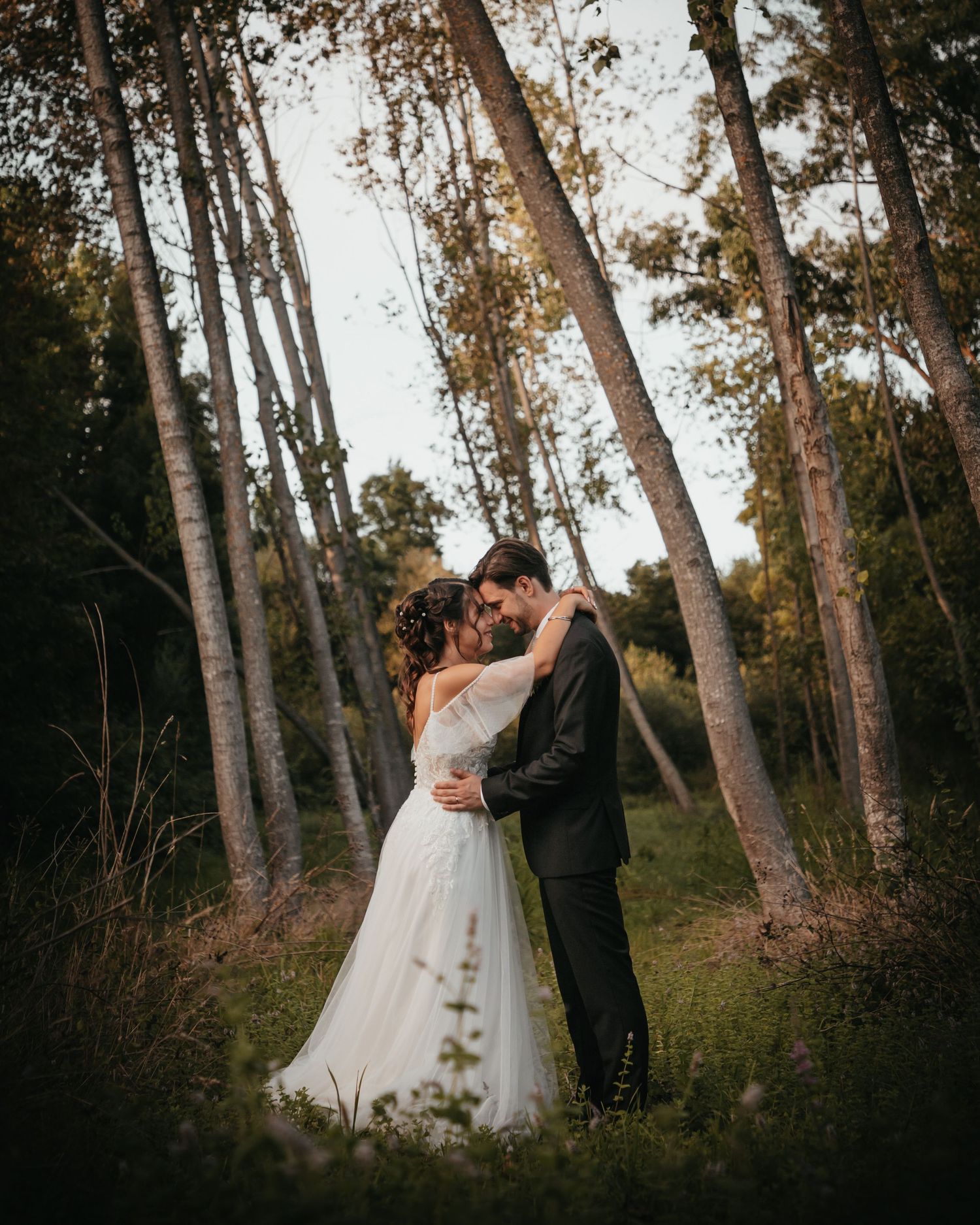 Dreamy wedding photo of couple embracing in a forest with tall pine trees.