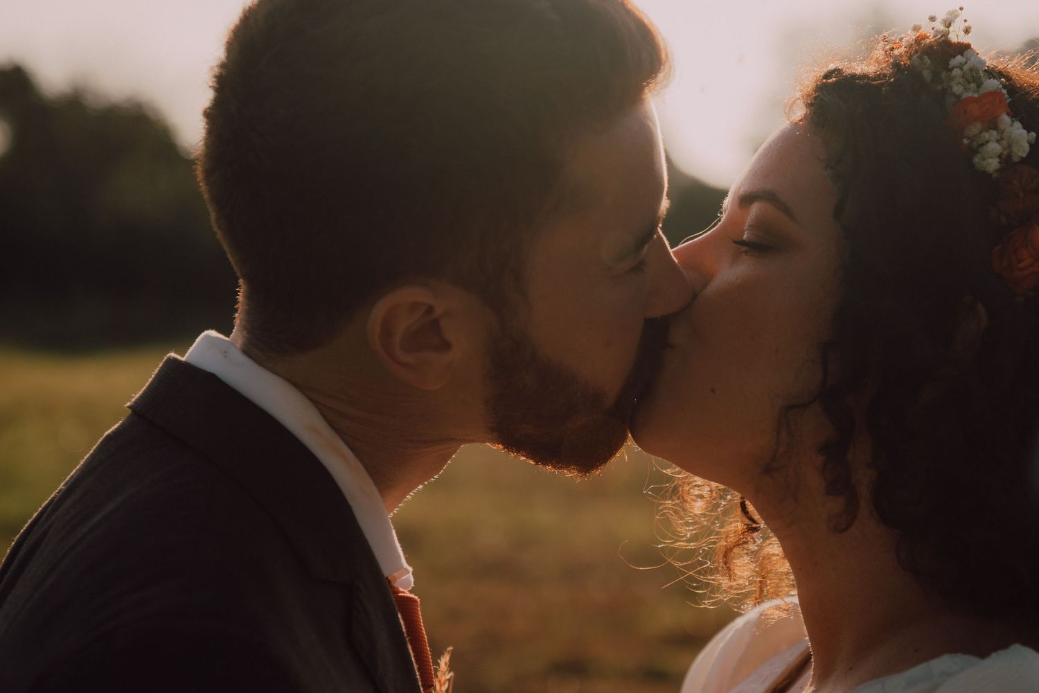 Romantic sunset kiss between newlyweds in golden hour lighting.