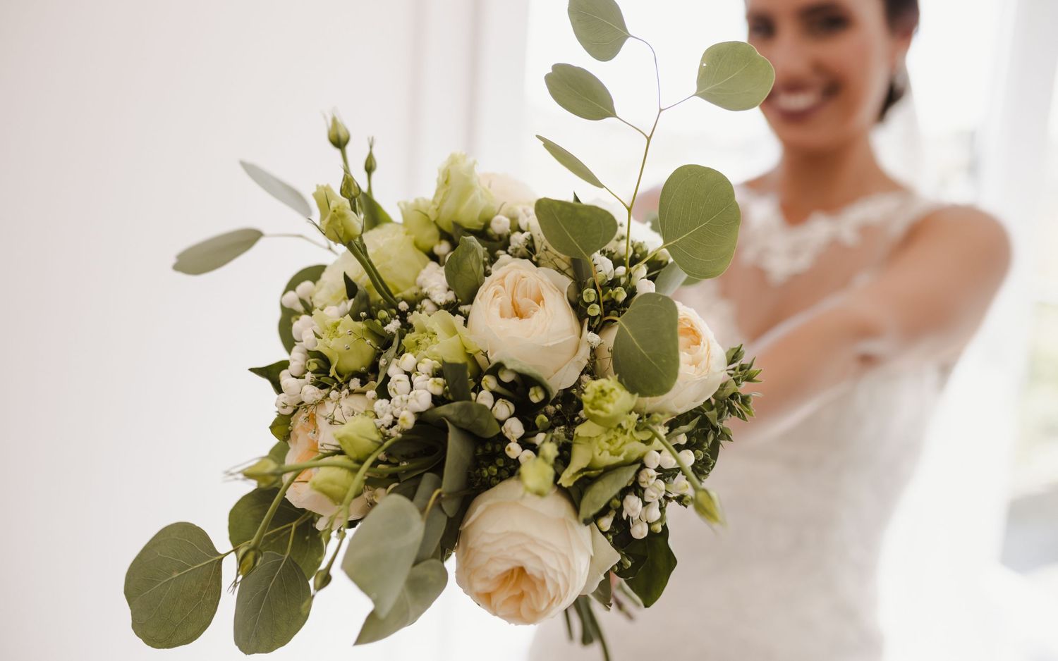 Elegant white and green wedding bouquet with roses and eucalyptus leaves in soft natural light.