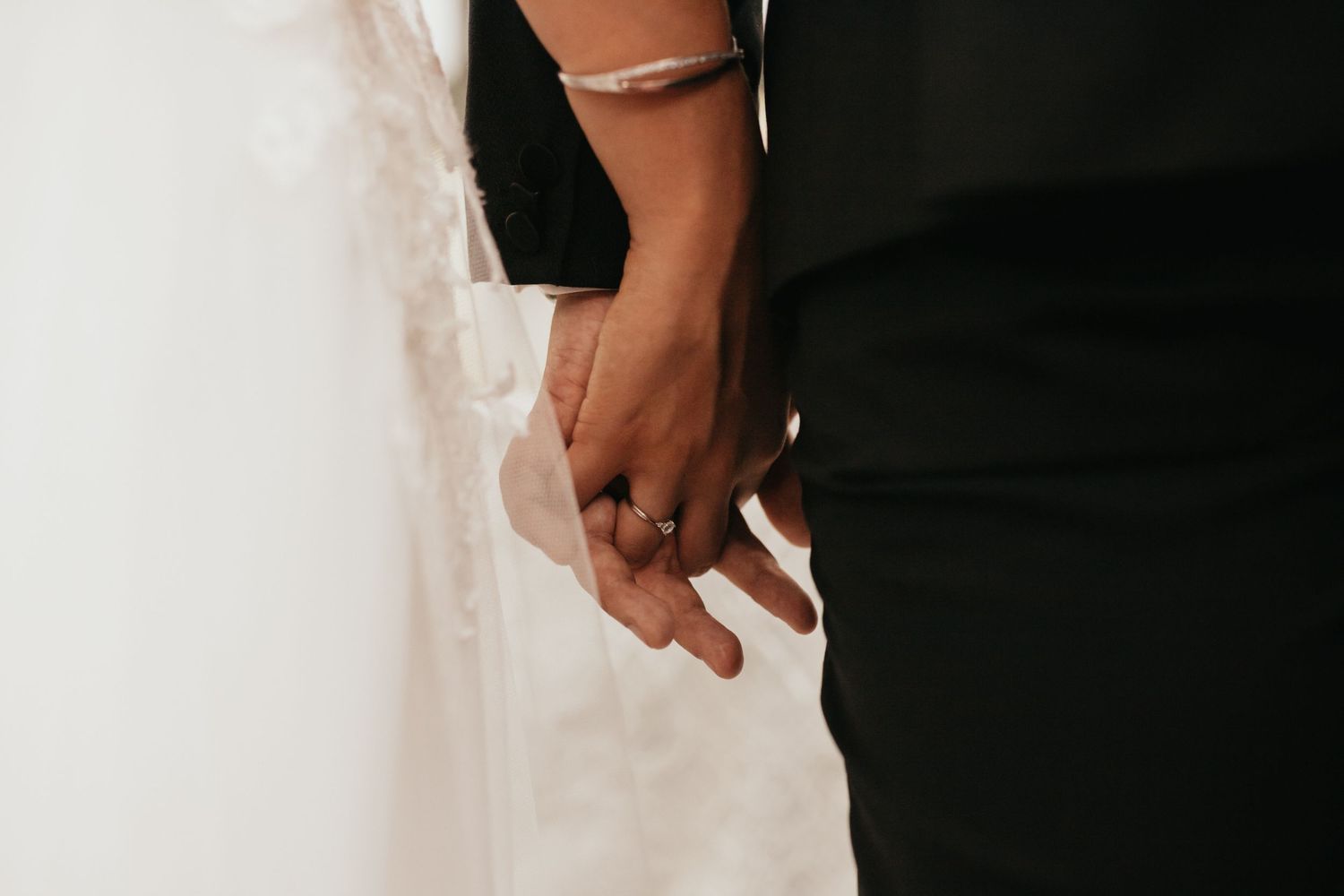 Close-up of couple holding hands showcasing wedding attire and rings.