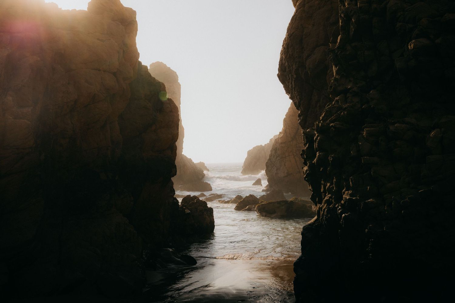 Dramatic rock formations frame a narrow ocean passage at sunset.