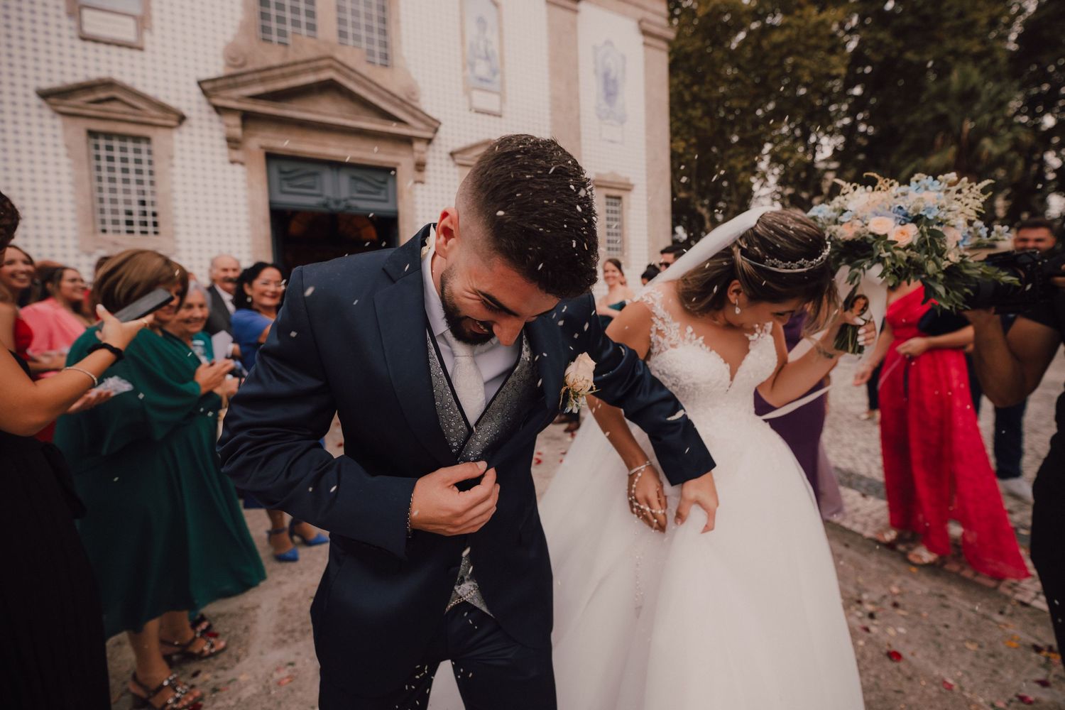 Wedding celebration outside a church with guests throwing confetti.