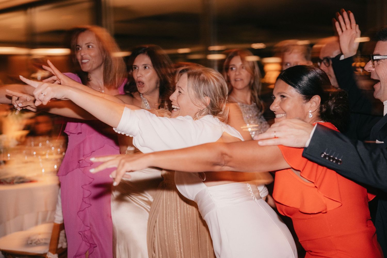 Wedding reception guests dancing and reaching out with arms extended on the dance floor.