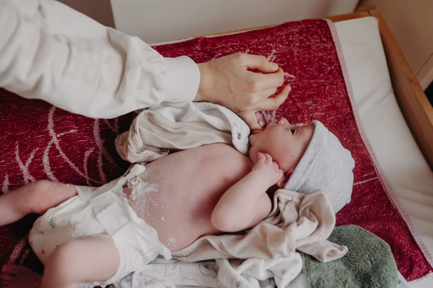 A newborn baby being gently swaddled in a white blanket on a red textured surface.