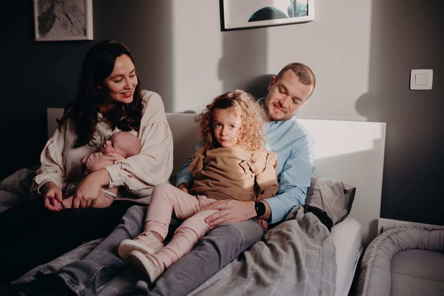 Family lounging together on a cozy grey couch in a dimly lit living room.