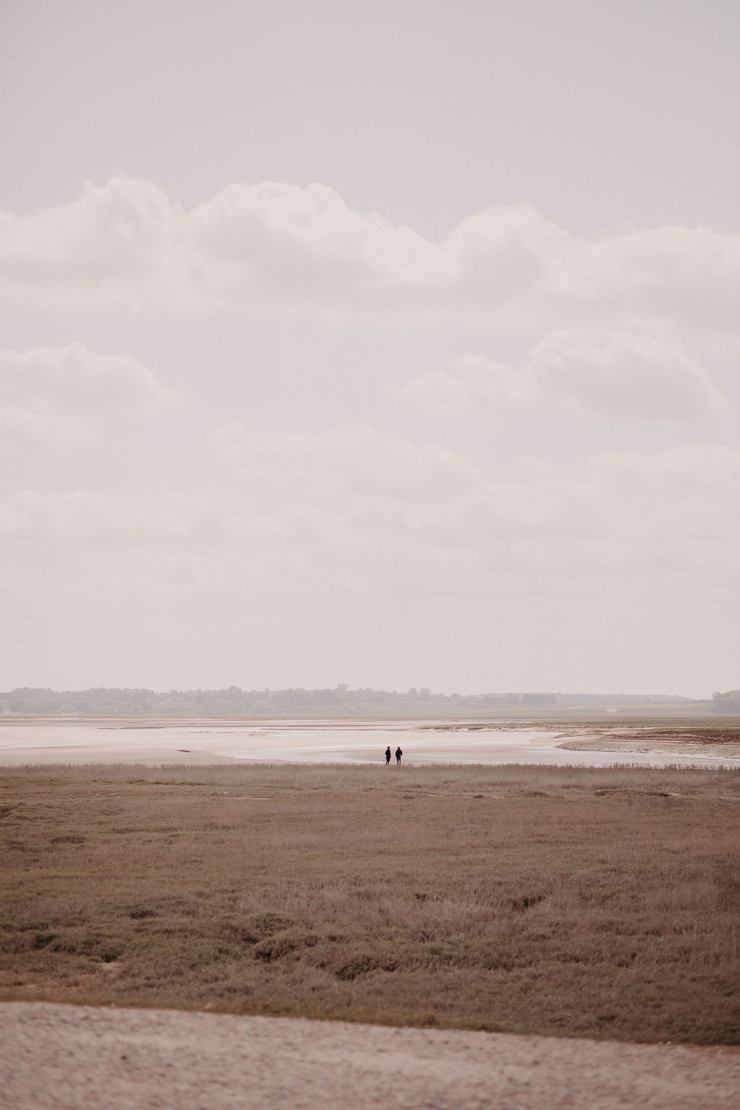 Two distant figures walking on a vast empty beach under moody overcast skies on a misty day.