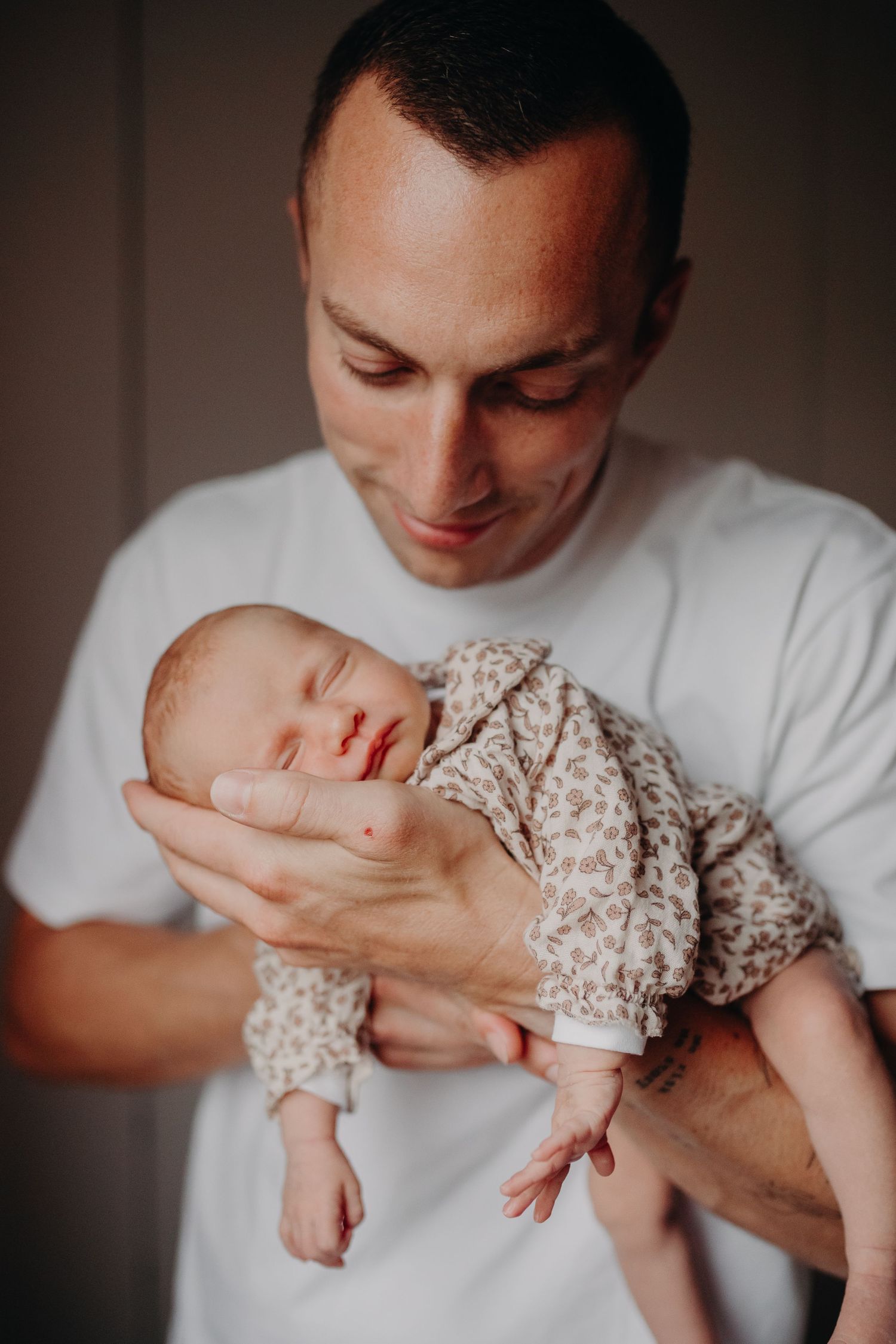 A tender moment captured as a person in a white t-shirt gently cradles a sleeping newborn baby in floral clothing.