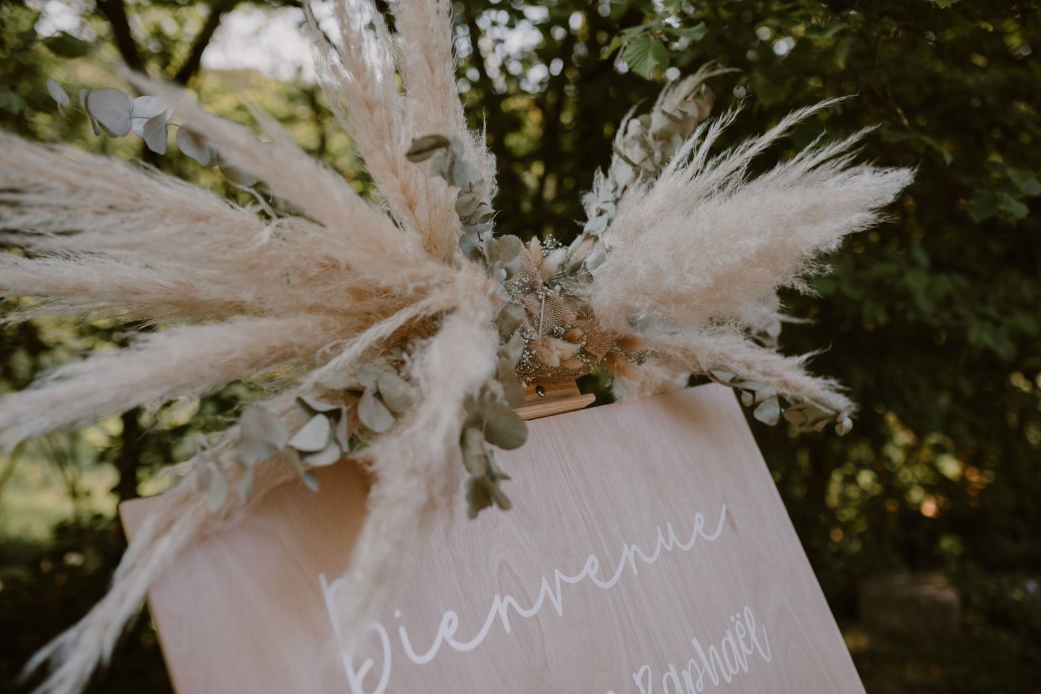 Delicate dried pampas grass and floral arrangement decorating a white paper sign with elegant calligraphy text.