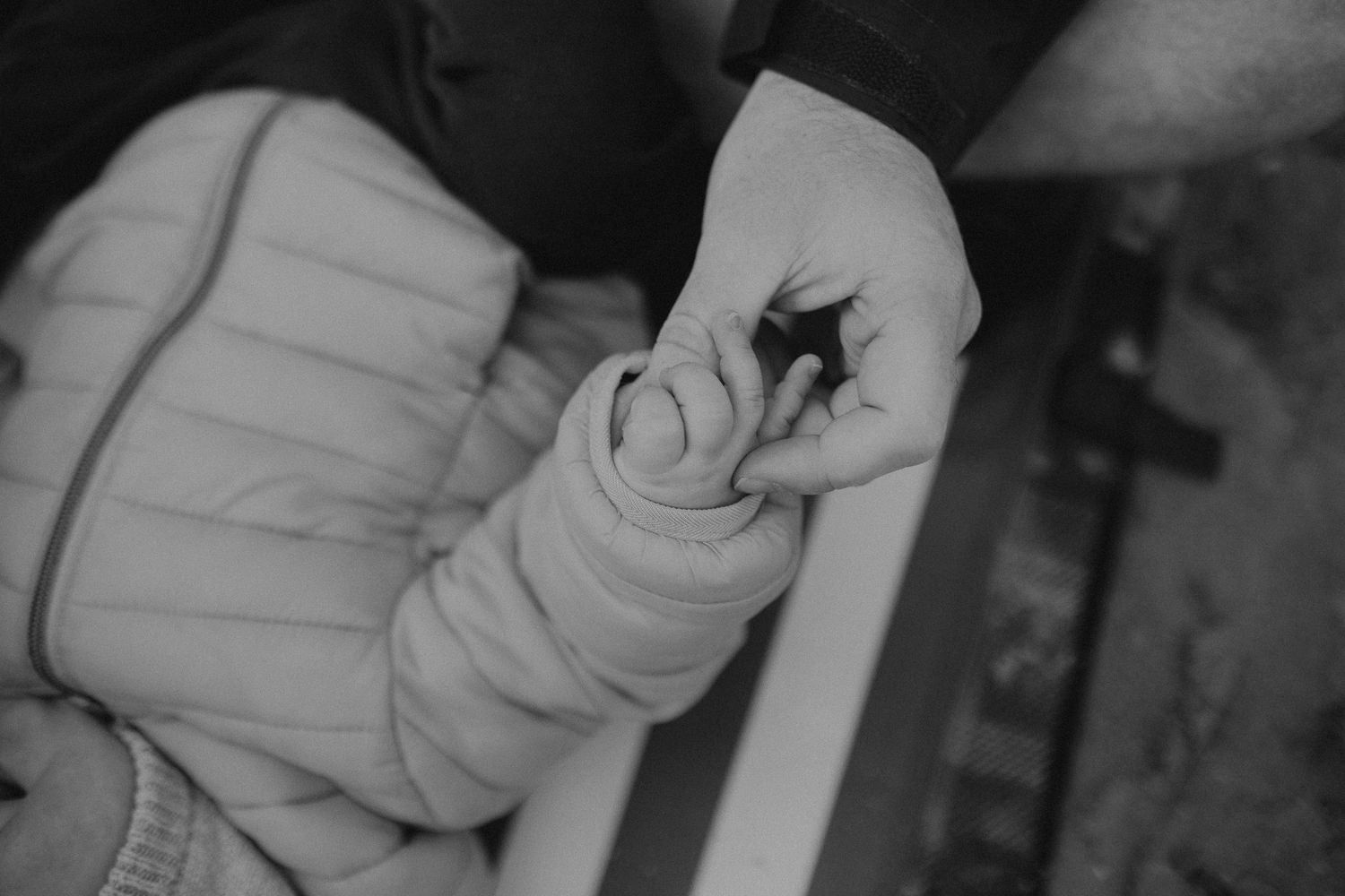 A close-up black and white photo shows a small hand grasping an infant's swaddled blanket.