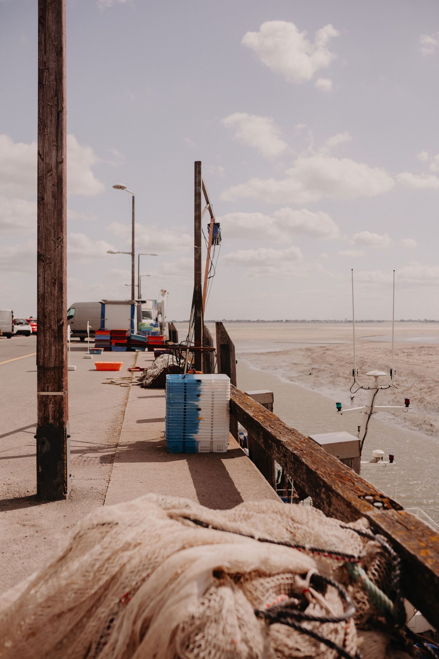 A weathered dock with barrels and posts overlooks a sandy beach under a cloudy sky.